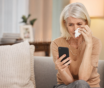 Buy stock photo Shot of a mature woman using a smartphone and crying on the sofa at home