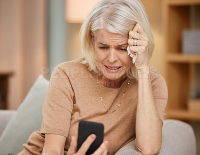 Buy stock photo Shot of a mature woman using a smartphone and crying on the sofa at home