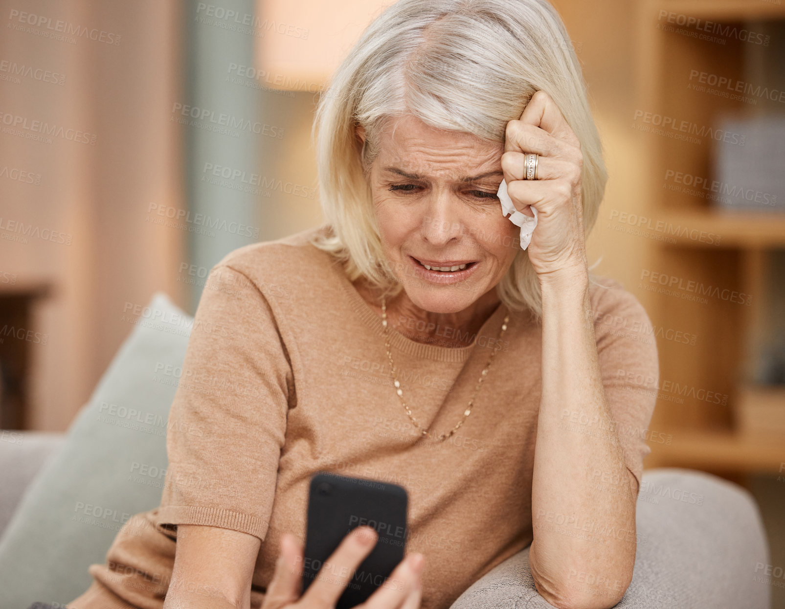 Buy stock photo Shot of a mature woman using a smartphone and crying on the sofa at home