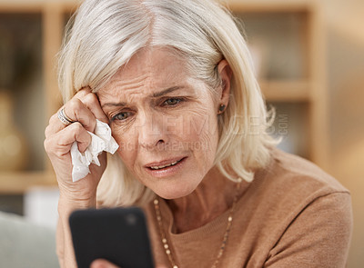 Buy stock photo Shot of a mature woman using a smartphone and crying on the sofa at home