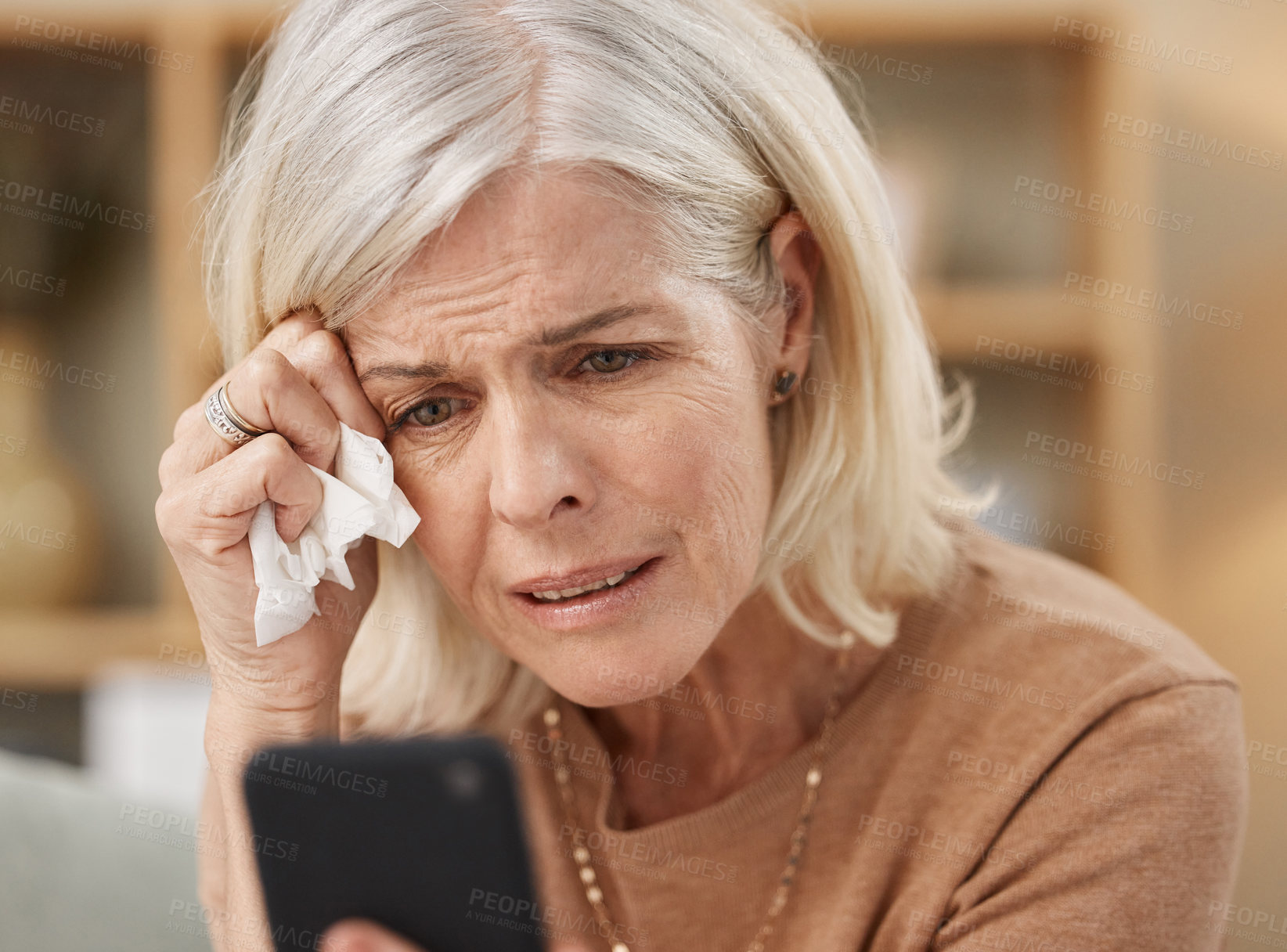 Buy stock photo Shot of a mature woman using a smartphone and crying on the sofa at home