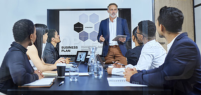 Buy stock photo Shot of a mature businessman using a digital tablet during a presentation to his colleagues in an office