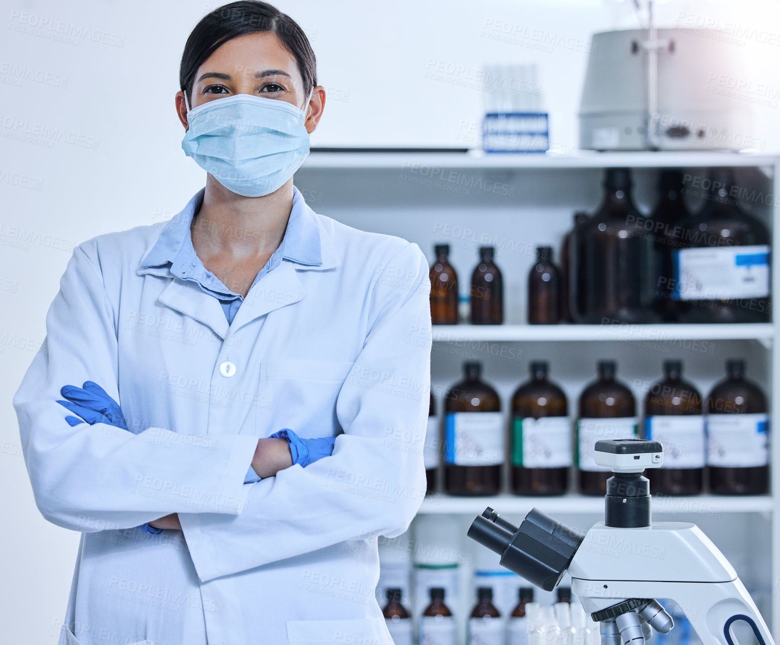 Buy stock photo Cropped portrait of a young female scientist wearing a mask while standing with her arms folded in her lab