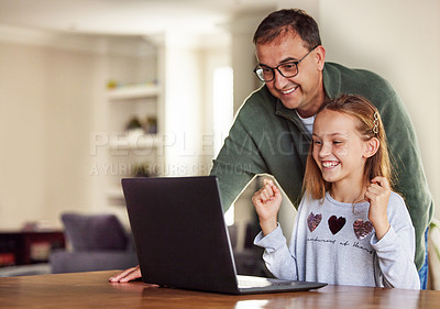 Buy stock photo Shot of an adorable little girl sitting and using a laptop at home while her father helps her