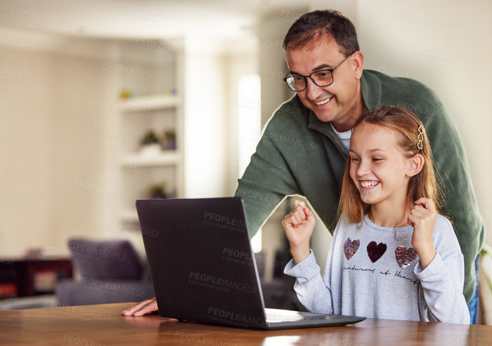 Buy stock photo Shot of an adorable little girl sitting and using a laptop at home while her father helps her