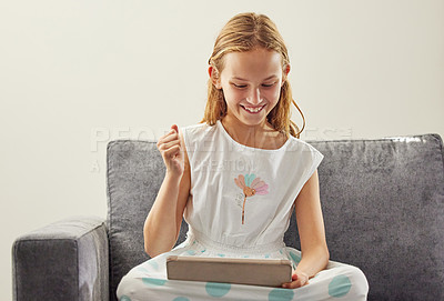 Buy stock photo Shot of an adorable little girl sitting alone on the sofa at home and using a digital tablet