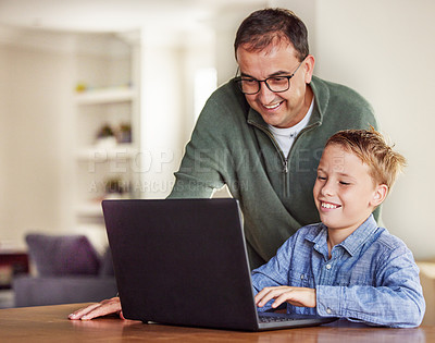 Buy stock photo Shot of an adorable little boy sitting and using a laptop at home while his father helps him