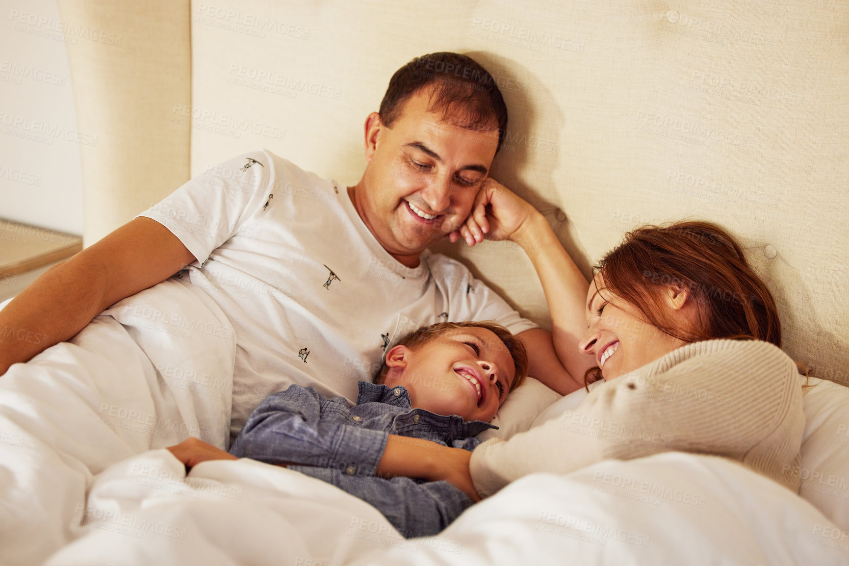 Buy stock photo Parents, child and wake up in bed, morning and happy with care, love and funny conversation in family home. Mother, father and son in bedroom, smile together and connection with comic chat in house