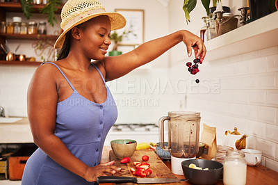 Buy stock photo Shot of an attractive young woman tossing fruit into a blender in the kitchen at home