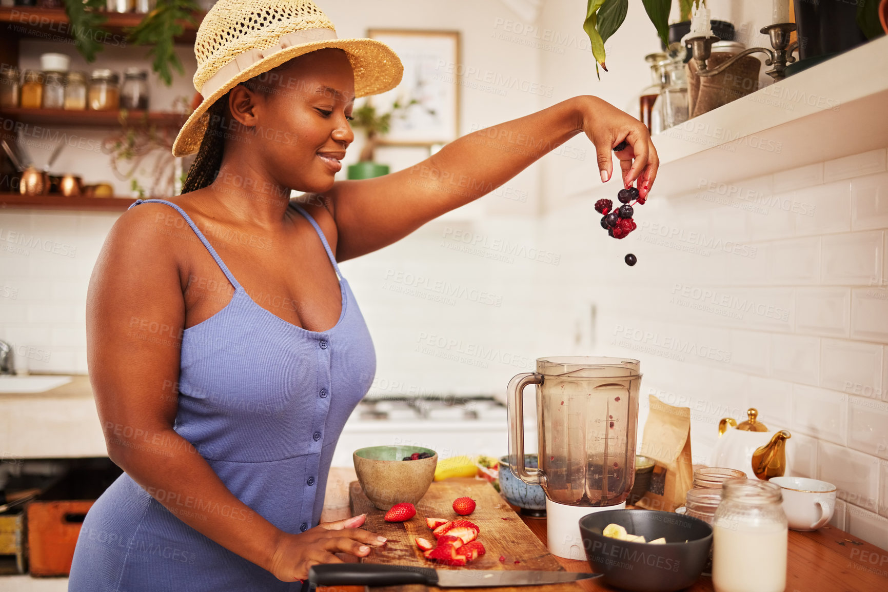 Buy stock photo Shot of an attractive young woman tossing fruit into a blender in the kitchen at home