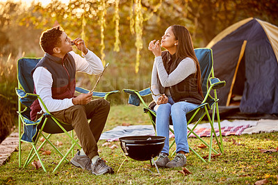 Buy stock photo Shot of a young couple roasting marshmallows while camping outside