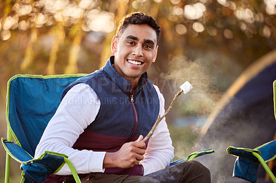 Buy stock photo Shot of a young man roasting marshmallows while camping outside