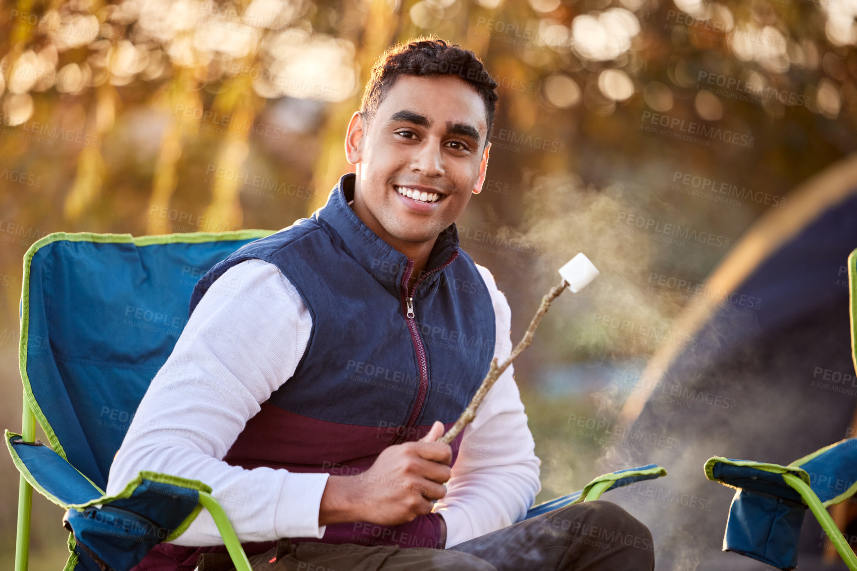 Buy stock photo Shot of a young man roasting marshmallows while camping outside