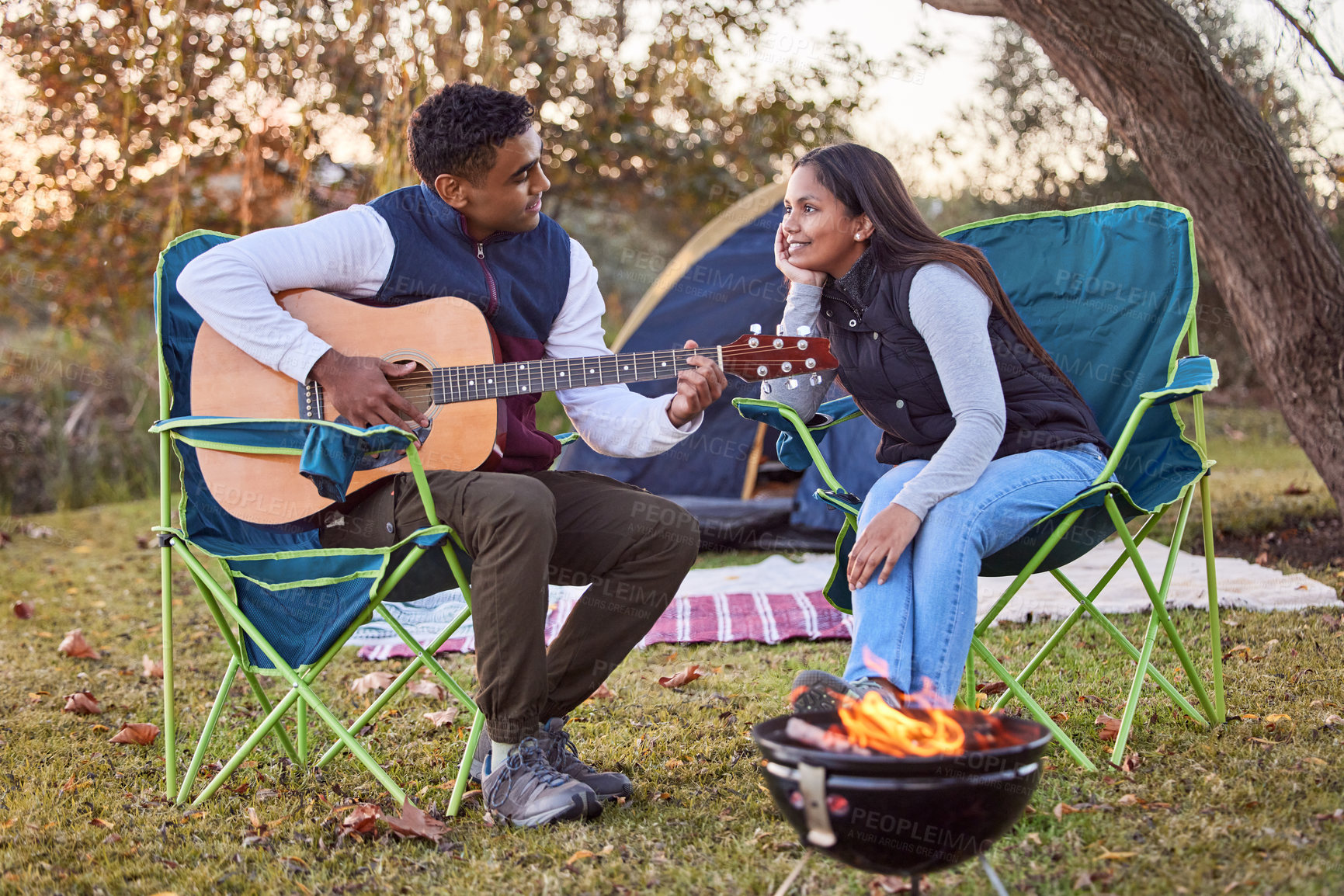 Buy stock photo Music, camping and couple with guitar in nature for romantic vacation, adventure or holiday. Love, singing and young man and woman playing song with string instrument by fire on outdoor weekend trip.