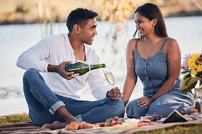 Buy stock photo Picnic, happy couple and love with champagne, glass and romantic date for anniversary outdoors. Eye contact, man or woman with alcohol to relax, celebrate and bond in relationship with snack by river