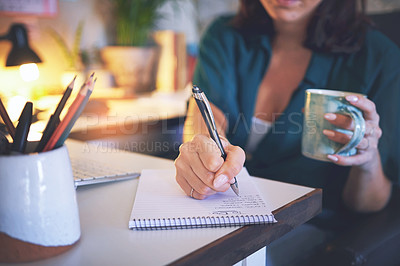 Buy stock photo Cropped shot of an unrecognizable woman sitting and enjoying a cup of coffee while writing notes in her home office