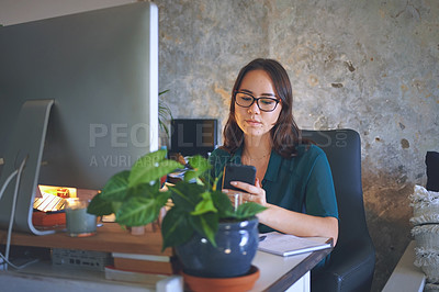 Buy stock photo Shot of an attractive young woman sitting alone and using her cellphone while working from home