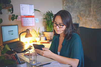 Buy stock photo Shot of an attractive young woman sitting alone and using her cellphone while working from home