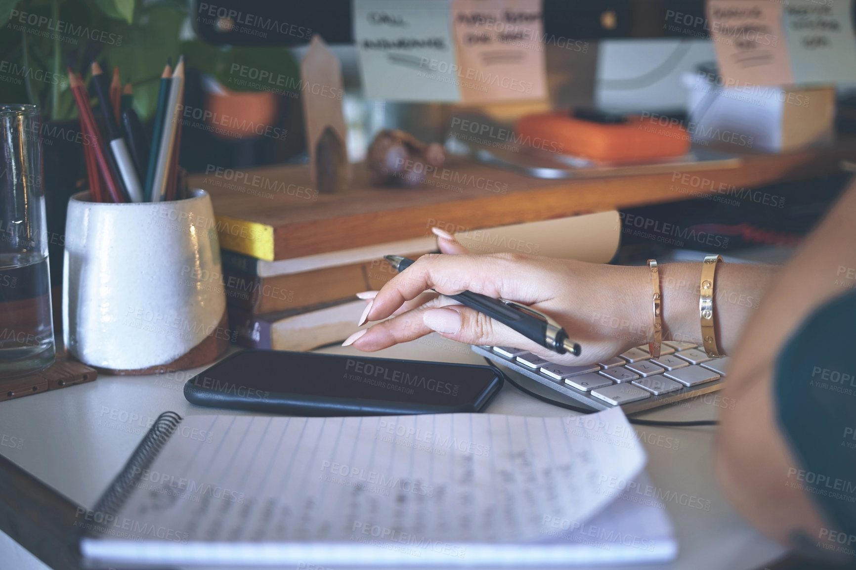 Buy stock photo Cropped shot of an unrecognizable woman sitting alone and using her cellphone while writing notes in her home office