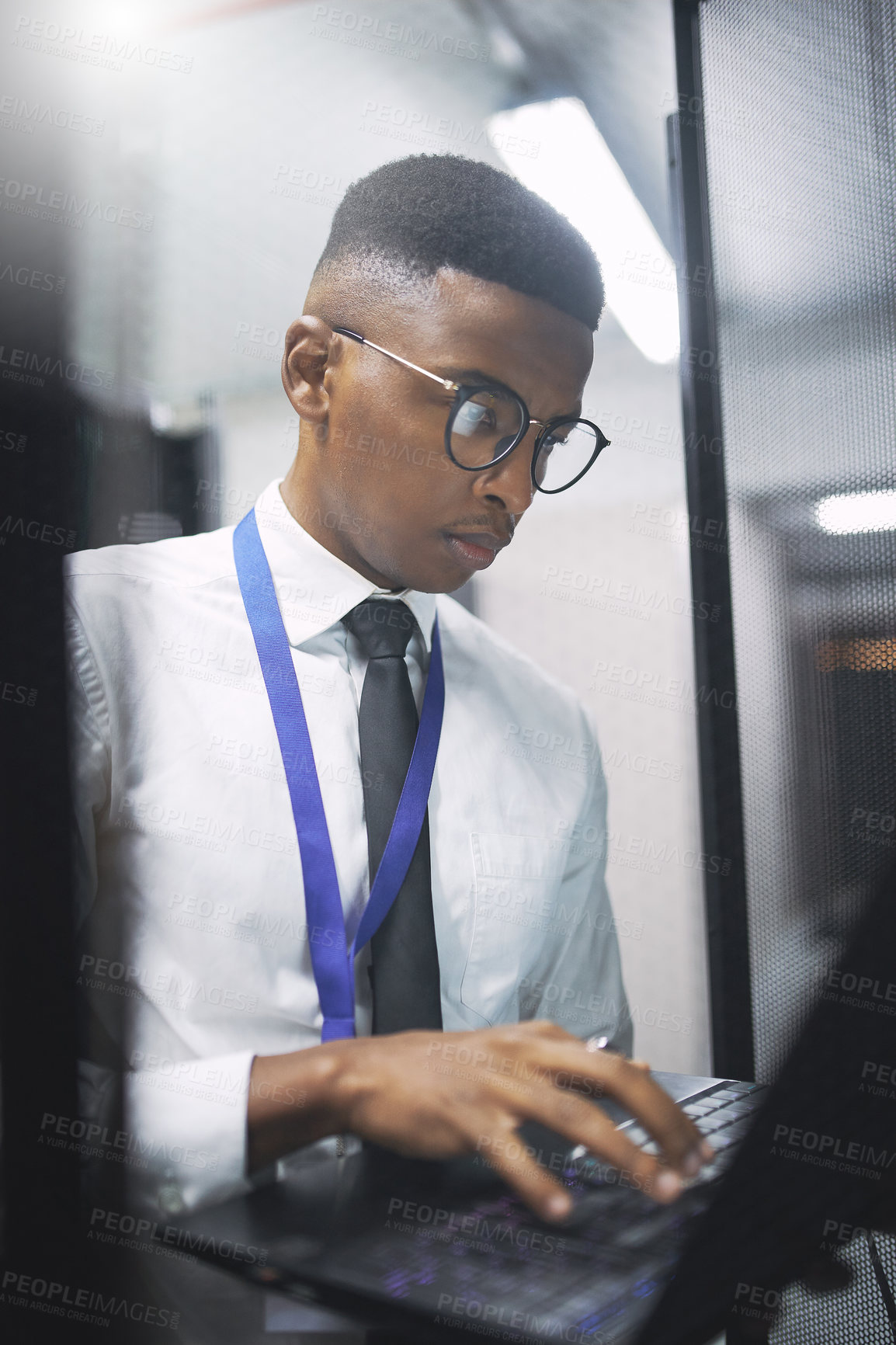 Buy stock photo Shot of a young male technician working in a server room