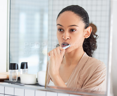 Buy stock photo Shot of an attractive young woman standing alone in her bathroom at home and brushing her teeth in the morning