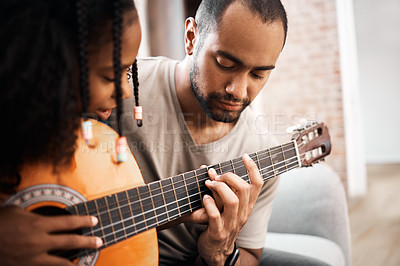 Buy stock photo Shot of a young girl learning to play the guitar with her father at home