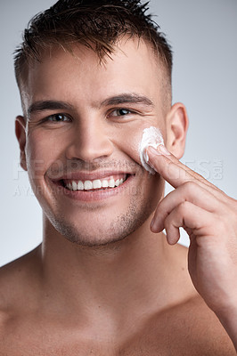 Buy stock photo Cropped closeup portrait of an attractive young man applying moisturiser to his face against a grey background