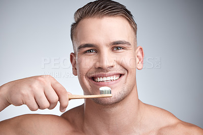 Buy stock photo Studio portrait of an attractive young man brushing his teeth against a grey background