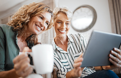 Buy stock photo Shot of two female friends drinking coffee while using a digital tablet