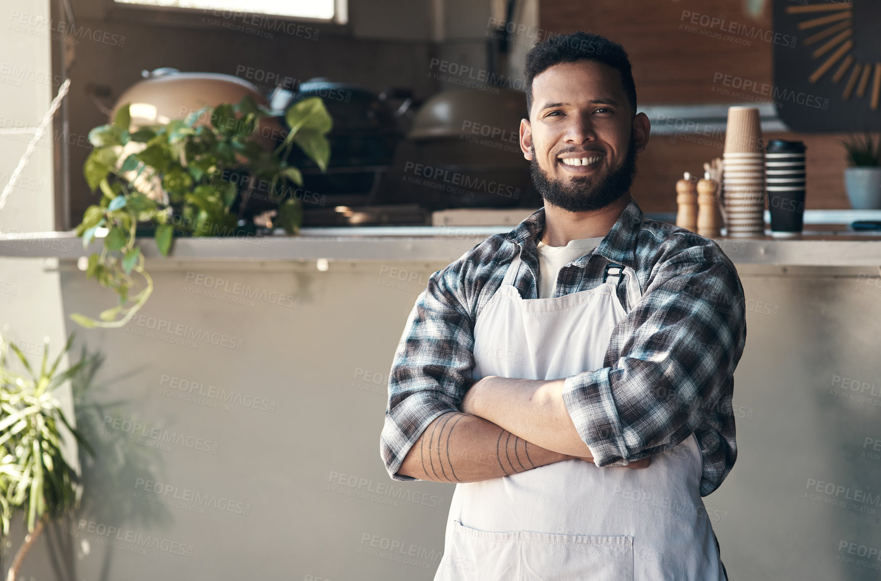 Buy stock photo Shot of a handsome young man standing outside his restaurant with his arms folded during the day