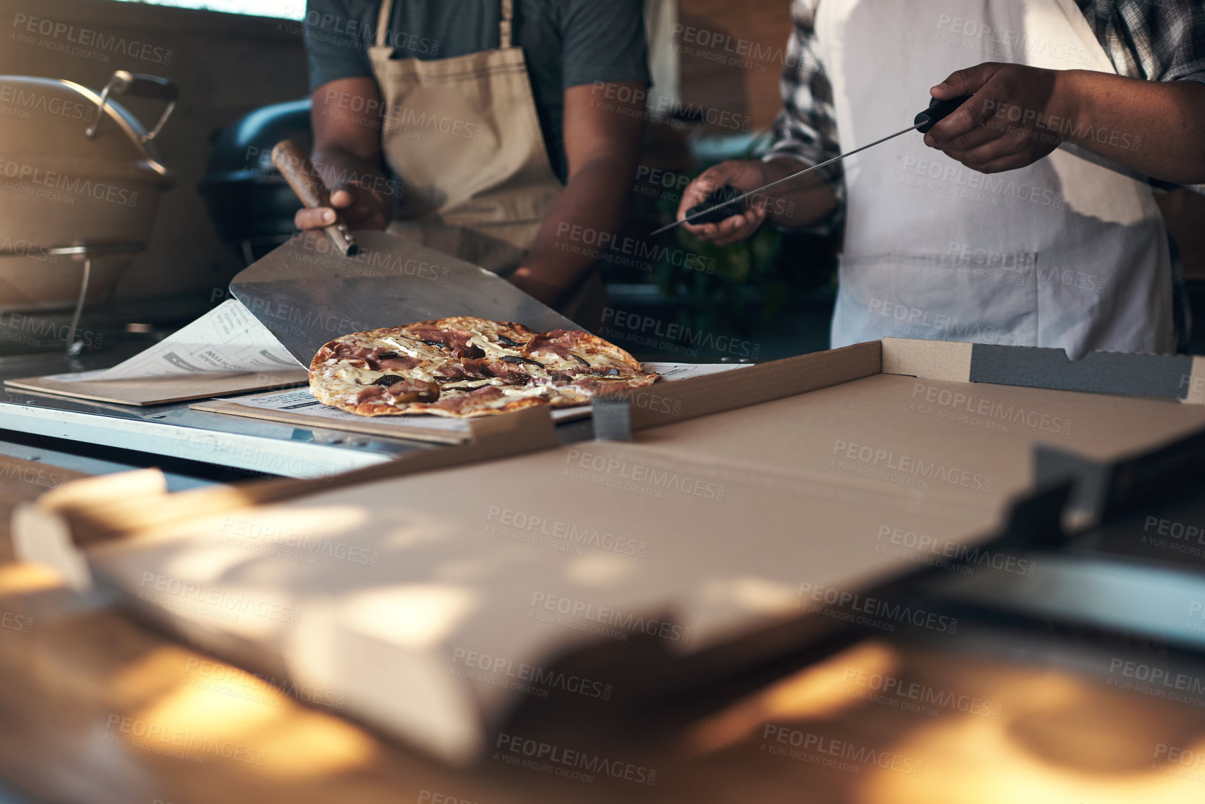 Buy stock photo Cropped shot of two unrecognizable men standing and preparing a freshly made pizza for takeaway in their restaurant