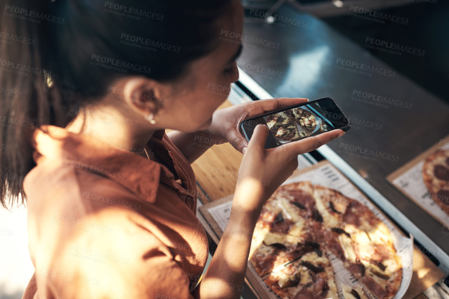 Buy stock photo Shot of an unrecognizable woman standing alone and using her cellphone to photograph her pizza at a restaurant