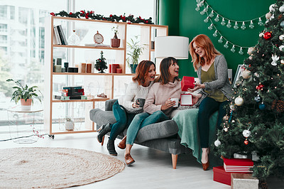 Buy stock photo Shot of three attractive woman exchanging Christmas gifts on the sofa at home