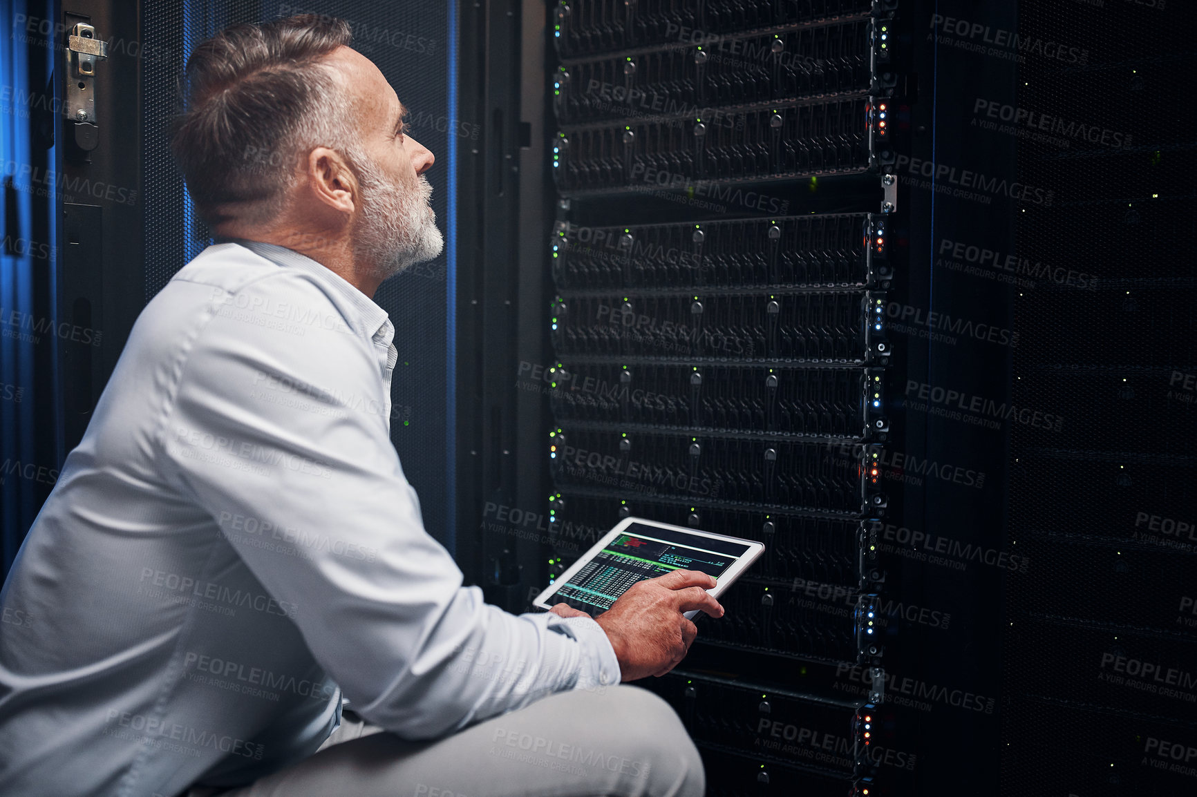 Buy stock photo Shot of a mature man using a digital tablet while working in a server room