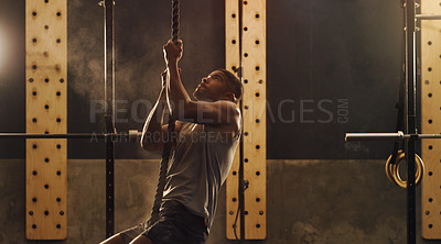 Buy stock photo Shot of a muscular young man climbing a rope in a gym