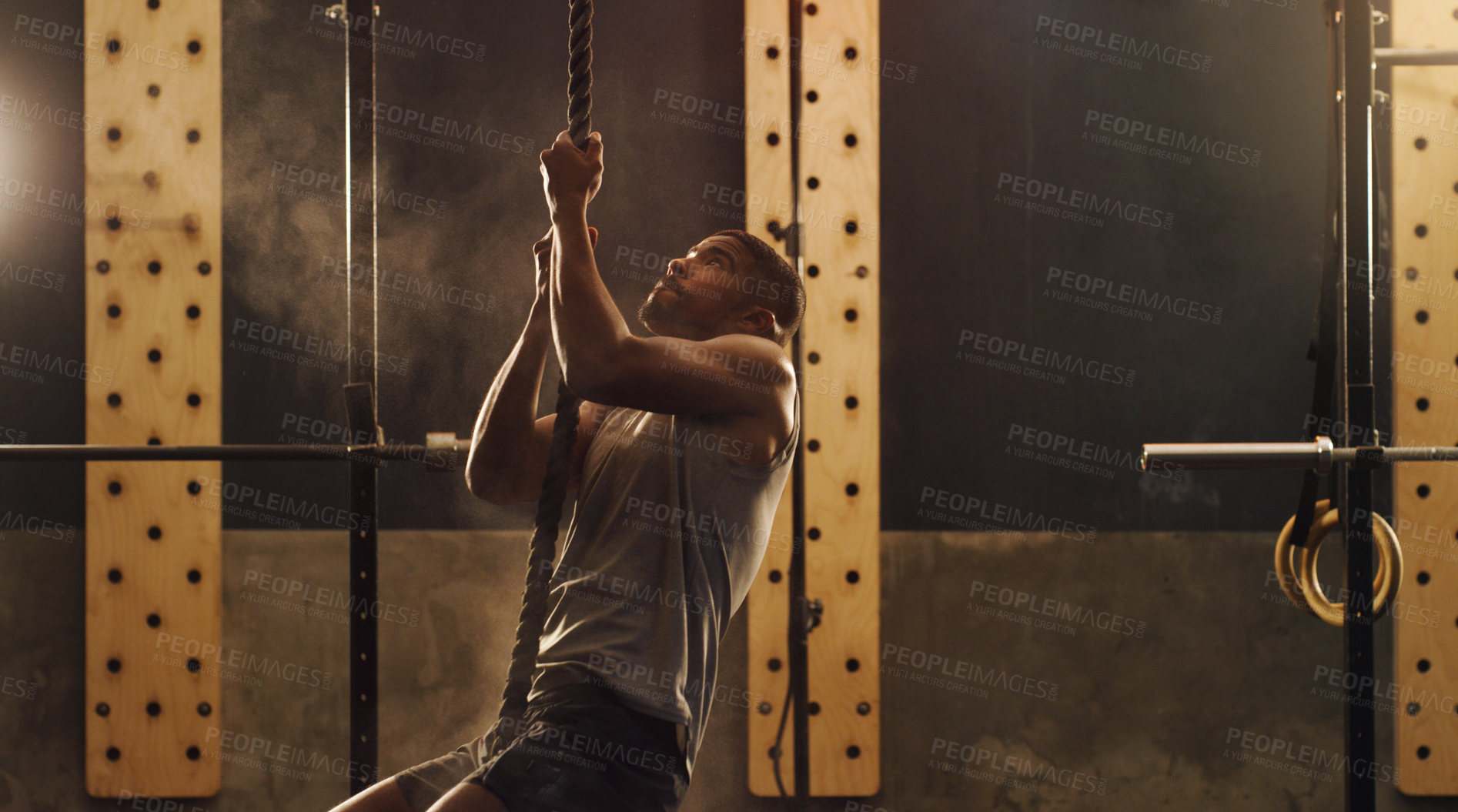 Buy stock photo Shot of a muscular young man climbing a rope in a gym