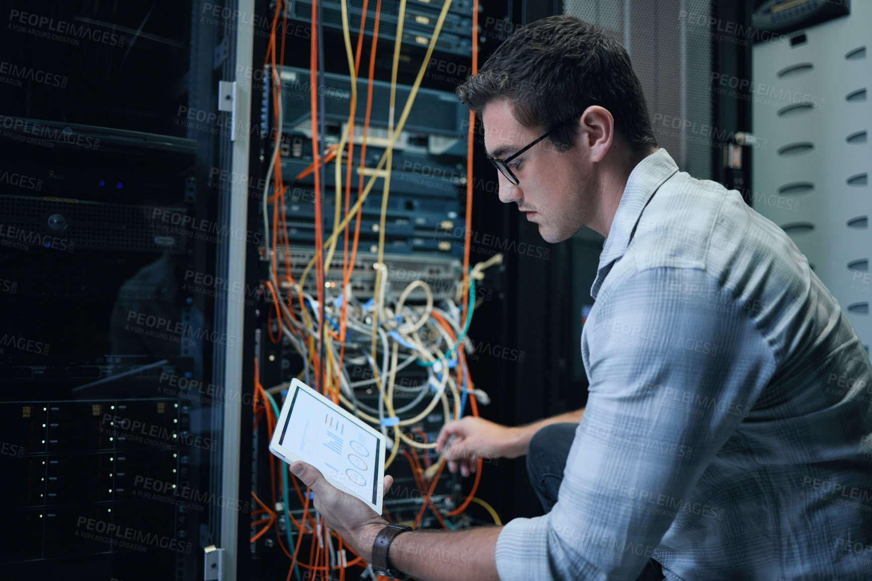 Buy stock photo Cropped shot of a handsome young male programmer working on a tablet in a server room