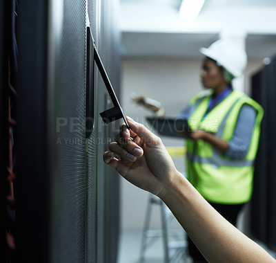 Buy stock photo Closeup shot of an unrecognizable female programmer working in a server room with a colleague in the background