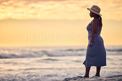 Buy stock photo Shot of an unrecognizable woman walking along the beach at sunset