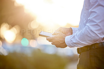 Buy stock photo Cropped shot of an unrecognizable businessman standing alone in the city and using his cellphone