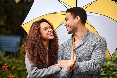 Buy stock photo Shot of a young couple standing in the rain with an umbrella