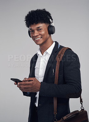 Buy stock photo Studio shot of a young businessman using a smartphone and headphones against a grey background