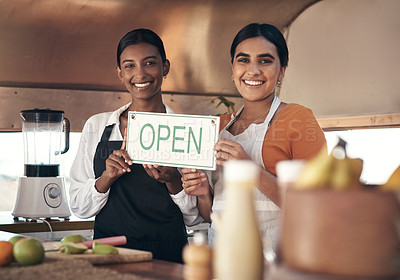 Buy stock photo Shot of two young businesswomen holding an open sign in their food truck