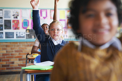 Buy stock photo Shot of a diverse group of children sitting in their school classroom and raising their hands to answer a question