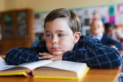 Buy stock photo Shot of a young boy sitting in his classroom at school and feeling bored