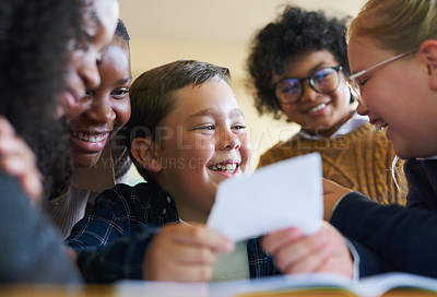 Buy stock photo Shot of a diverse group of children huddled together in their school classroom and laughing while reading a note