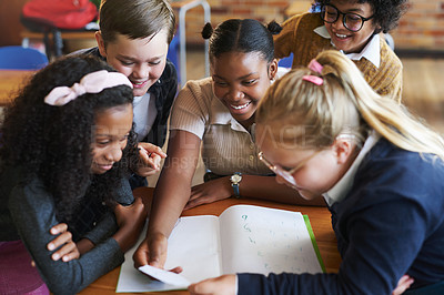 Buy stock photo Shot of a diverse group of children huddled together in their school classroom and reading a note