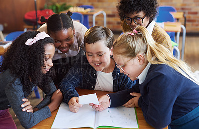 Buy stock photo Shot of a diverse group of children huddled together in their school classroom and reading a note