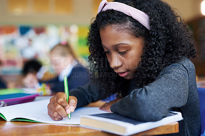 Buy stock photo Shot of a young girl sitting in her classroom at school and writing in her workbook