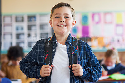 Buy stock photo Shot of a young boy standing in his classroom at school and holding his backpack